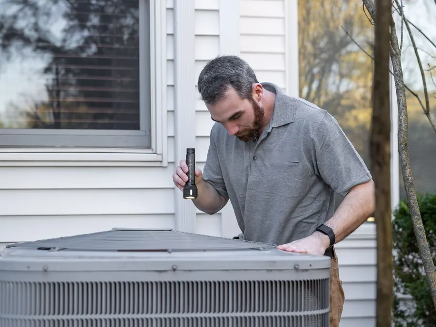 HVAC technician inspecting an outdoor air conditioner beside a home